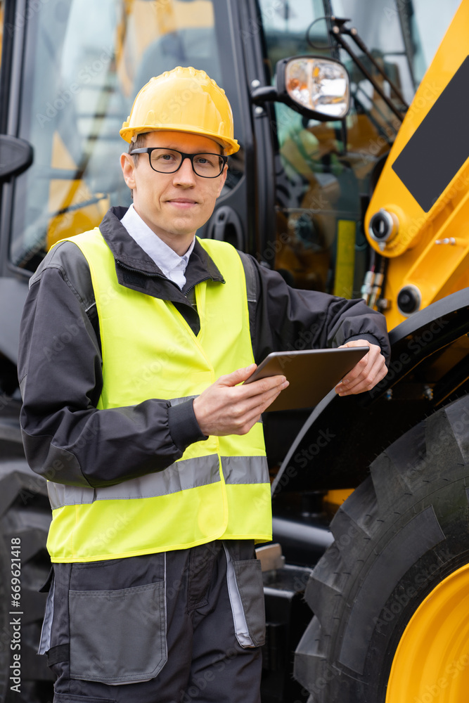 Aufkleber engineer in a helmet with a digital tablet stands next to construction excavators.