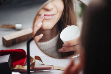 Woman using vaseline on her mouth. Closeup lips background. Applying vaseline on lips with finger. Beauty background. Young girl skin care. Cosmetics for moisturize. Table mirror face reflection. - obrazy, fototapety, plakaty