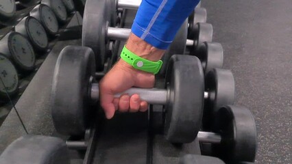 Man hand takes dumbbell out of set of black weights. Sports training and dumbbell weight selection
