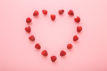 Heart shape created from red fresh raspberries on light pink table background. Pastel color. Love healthy food. Closeup. Top down view.