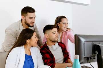 Young woman in glasses points at PC monitor and the group looks attentively. Labor office concept. Hipster group concept.