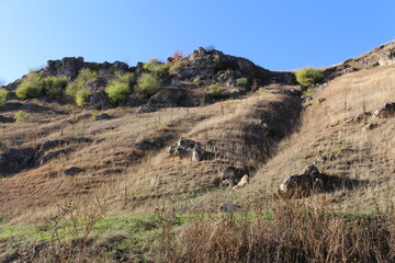 Fototapeta na wymiar A rocky hillside with a grassy hill and a blue sky