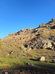 A grassy hill with rocks and a blue sky