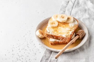 Toasts with butter, banana slices and honey on light linen background. Homemade breakfast sandwich close up. Simple food concept