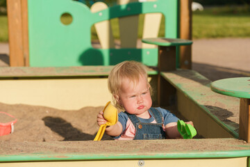 Cute baby kid sit in the sandbox and play with sand in a public park