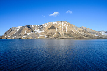 Peaceful sunny blue landscape of arctic ocean, rocky mountain range with snow, and blue sky,...