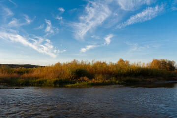 Beautiful autumn landscape with blue sky with clouds a river and trees