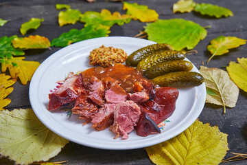 Slowly roasted smoked pork knuckle in dark beer served on the vintage plate with pickled cucumbers and rustic style mustard. Traditional autumn seasonal dish from bavarian, austrian or czech cuisine