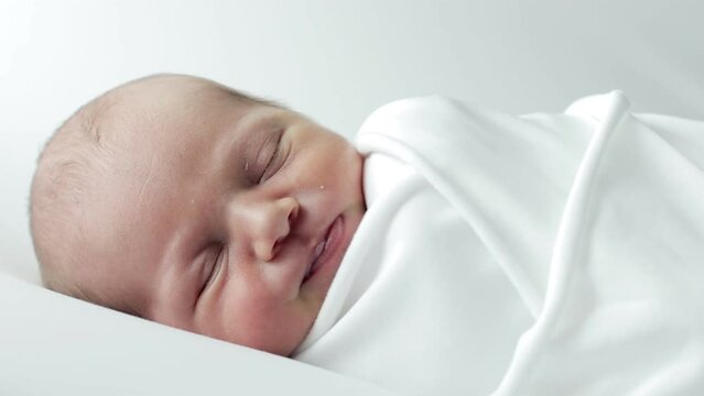 A 3-day-old baby wrapped in white cloth sleeping on a white background.