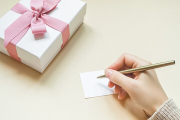 female hand signs a greeting card on the background of a gift box