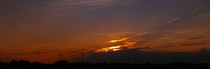 Sunset with a dramatic sky and overland high voltage lines near Tabertshausen, Deggendorf, Bavaria, Germany