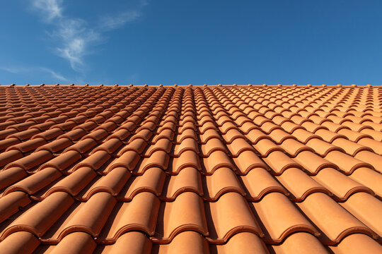 Clay tile roof close-up. New roofing made of orange clay tiles with blue sky in the background, free space for text, copy space