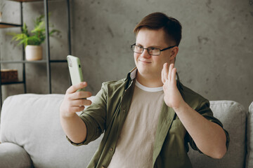 Young man with down syndrome in glasses casual clothes do selfie shot mobile cell phone sit on grey...