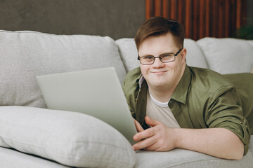 Young IT man with down syndrome wears glasses casual clothes work use laptop pc computer lay on...