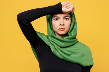 Young sad sick ill arabian asian muslim woman wearing green hijab abaya black clothes put hand on forehead suffer isolated on plain yellow background People uae middle eastern islam religious concept
