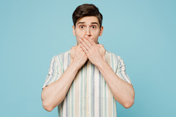 Young sad astonished scared man he wearing striped shirt casual clothes looking camera covers mouth with hands isolated on plain pastel light blue cyan background studio portrait. Lifestyle concept.