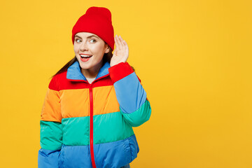Young curious nosy woman she wears padded windbreaker jacket red hat casual clothes try to hear you overhear listening intently isolated on plain yellow background studio portrait. Lifestyle concept. - obrazy, fototapety, plakaty