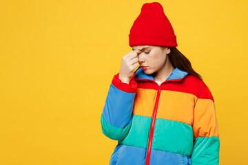 Young sad sick ill woman tired she wears padded windbreaker jacket red hat casual clothes keep eyes closed rub put hand on nose isolated on plain yellow background studio portrait. Lifestyle concept. - obrazy, fototapety, plakaty