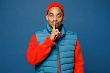 Young man of African American ethnicity wear padded vest red hat say hush be quiet with finger on...