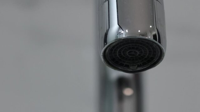 Metal faucet nozzle dripping water droplets close up macro shot. 