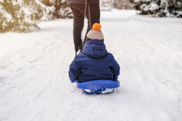 Blurred background with dad takes his son on a sled through the snow in the park