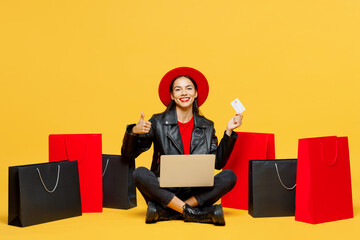 Full body young woman wear casual clothes red hat sit near shopping package bags hold credit card...