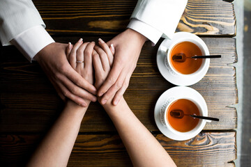Intimate Moment of Couple Holding Hands Over Tea on Wooden Table