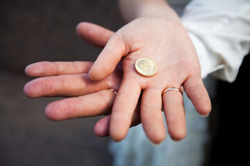 Bride and Groom's Hands Together Holding a Coin with Heart Symbol Close-Up