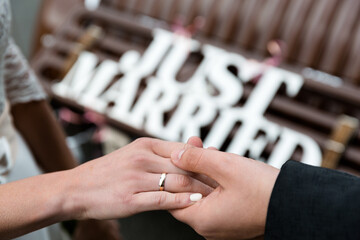 Close-up of Newlyweds' Hands with Rings Against 'Just Married' Sign