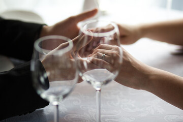 Close-up of Hands Holding Over Empty Wine Glasses with an Engagement Ring Visible