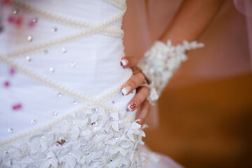 Bride's hand with manicured nails on embellished wedding dress.