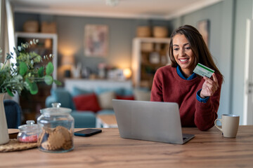 Beautiful smiling businesswoman doing online shopping over laptop with credit card at desk in home...