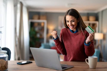 Fotobehang Enthusiastic charming millennial woman feeling excited looking at laptop screen holding credit card, raising fist in yes gesture satisfied with online payment possibilities, rejoicing approved loan. © Dorde