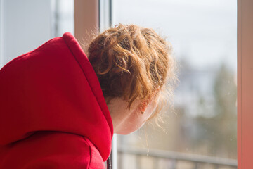 a woman in a red hoodie looks out of the window with a serious look of concentration