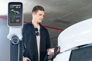 Young man travel with EV electric car to shopping center parking lot charging in downtown city...