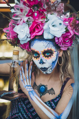 Mexican woman dressed and characterized as a catrina for the Day of the Dead festivity, in her hands she carries a bottle of mezcal with a scorpion inside, behind her a background  of mezcal bottles.