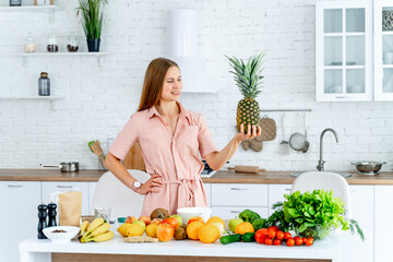 Woman in Kitchen Delightfully Posing With Tropical Fruit. A woman standing in a kitchen holding a pineapple - Powered by Adobe
