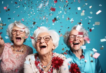 three happy senior women at new year party with confetti dancing on blue background, celebrating holiday season or birthday