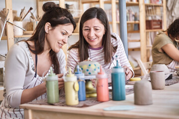 Two women painting ceramic crafts in a pottery workshop. Hobby and craft concept.