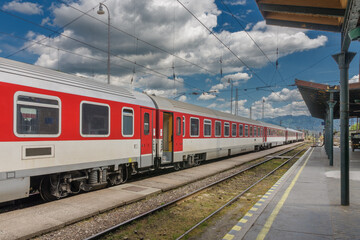 Red train in train station, empty platform, on background Slovakia mountains.