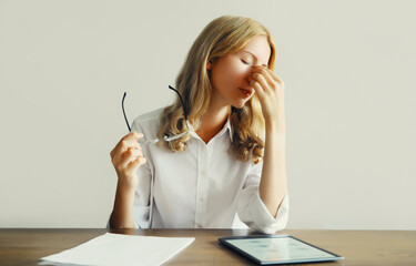 Tired overworked young woman rubbing her eyes suffering from eye strain, dry eye syndrome or headaches after working at the computer for a long time while sitting at desk in office or home