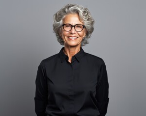 An elderly successful woman with glasses on a dark background in a black stylish blouse smiles. Success and career, successful woman.