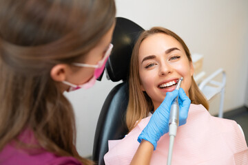 An attractive young woman is having her teeth professionally cleaned and cared for at a stomatology clinic. 