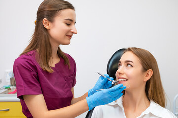 Cheerful female dentist holding dentist tool near smiling young patient.