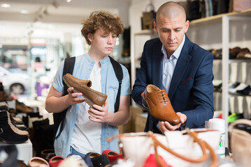 Fototapeta na wymiar Man visiting shoe shop with teenage son in search of comfortable elegant formal shoes .