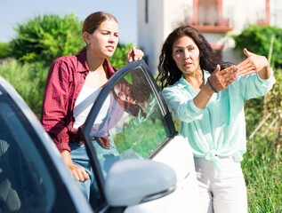 Young woman got out of her car and asking way to destination. She's talking with Asian woman who's gesticulating and explaining way to her.
