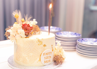 Mom's 50th birthday cake with lighted candle and plates background blur selective focus noise