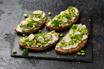 Soya bean and goats cheese sourdough bruschetta served with lemon zest and reddish on black slate board