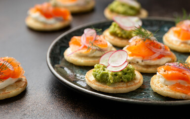 Mini blini pancakes with soft cheese, cold smoked salmon and guacamole