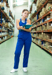 Attentive female manager keeps records of construction materials in big warehouse, writing down data on paper